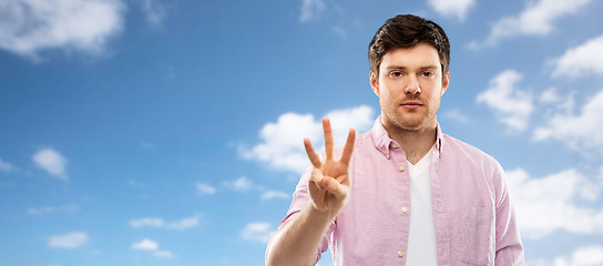 Image showing young man showing three fingers over sky