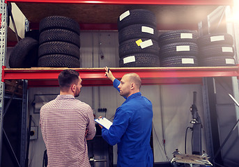 Image showing auto mechanic and man with tires at car shop