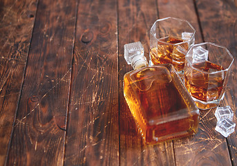 Image showing Bottle of whiskey with two glasses placed on rustic wooden table