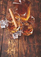 Image showing Bottle of whiskey with two glasses and cuban cigar placed on rustic wooden table