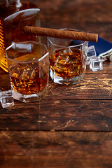 Image showing Bottle of whiskey with two glasses and cuban cigar placed on rustic wooden table