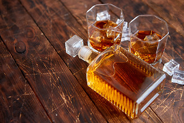 Image showing Bottle of whiskey with two glasses placed on rustic wooden table