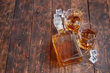 Image showing Bottle of whiskey with two glasses placed on rustic wooden table