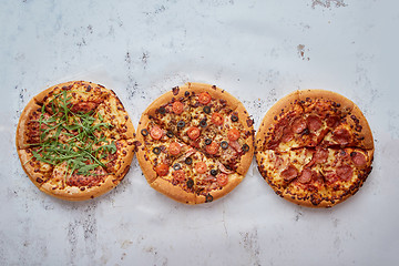 Image showing Three different kind of pizzas placed in a row on white rusty ta