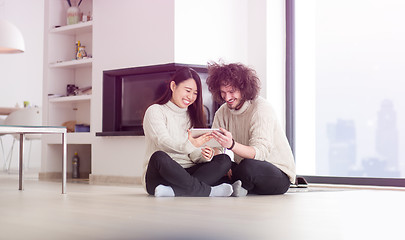 Image showing multiethnic couple using tablet computer in front of fireplace