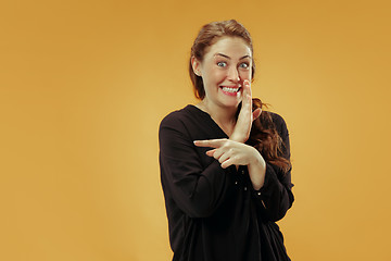 Image showing The young woman whispering a secret behind her hand over studio background