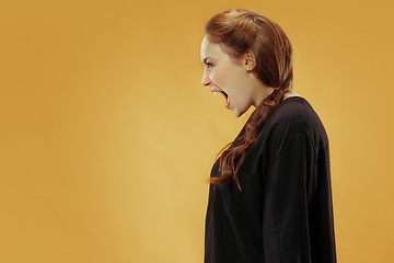 Image showing The young emotional angry woman screaming on gold studio background