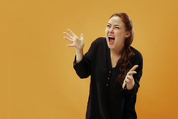 Image showing The young emotional angry woman screaming on gold studio background