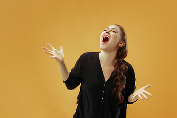 Image showing The young emotional angry woman screaming on gold studio background