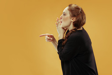 Image showing The young woman whispering a secret behind her hand over gold background