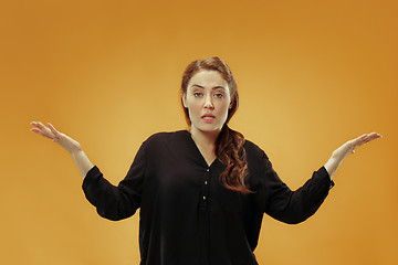 Image showing Beautiful female half-length portrait isolated on gold studio backgroud. The young emotional surprised woman