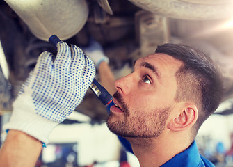 Image showing mechanic man with flashlight repairing car at shop