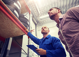 Image showing auto mechanic and man with tires at car shop