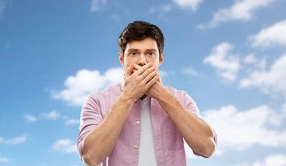 Image showing shocked man covering mouth by hands over blue sky