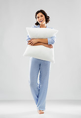 Image showing happy young woman in blue pajama hugging pillow