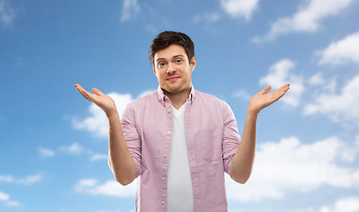 Image showing young man shrugging over blue sky background