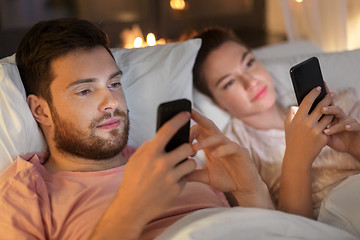 Image showing couple using smartphones in bed at night