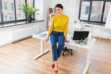 Image showing happy businesswoman sitting on desk at office