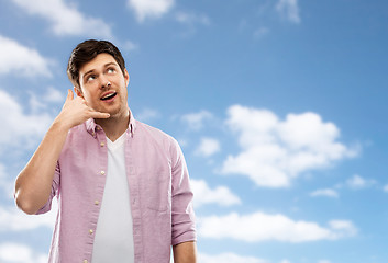 Image showing young man showing phone call gesture over blue sky