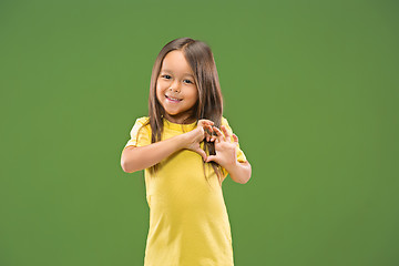 Image showing Beautiful smiling teen girl makes the shape of a heart with her hands on the green background.