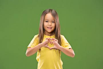 Image showing Beautiful smiling teen girl makes the shape of a heart with her hands on the green background.