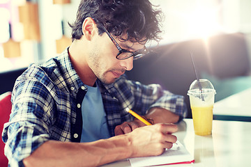 Image showing man with notebook and juice writing at cafe