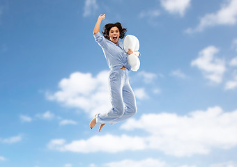 Image showing happy woman in pajama jumping with pillow over sky