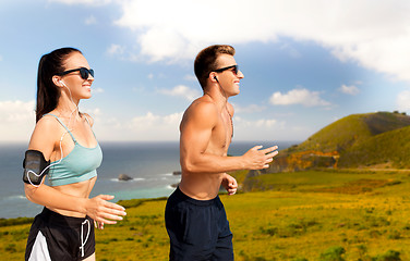 Image showing couple with phones and arm bands running on beach