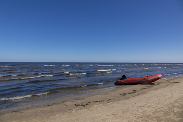 Image showing Rubber boat on a sand seashore on a blue sky background.