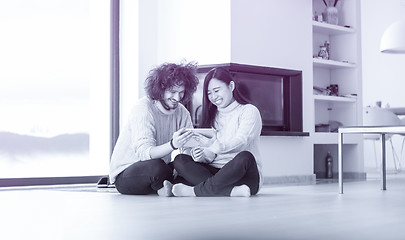 Image showing multiethnic couple using tablet computer in front of fireplace