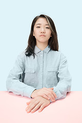 Image showing The serious business woman sitting and looking at camera against blue background.