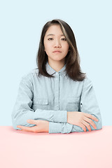 Image showing The serious business woman sitting and looking at camera against blue background.