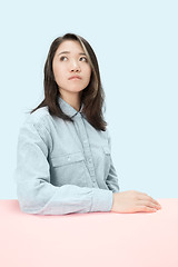 Image showing The serious business woman sitting and looking up against blue background.