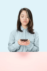 Image showing The serious business woman sitting and looking at phone against blue background.