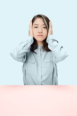 Image showing portrait of stressed woman sitting at table with closed and covering her ears with hands.