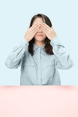 Image showing Young woman sitting at table at studio with eyes closed isolated on blue