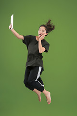 Image showing Image of young woman over green background using laptop computer or tablet gadget while jumping.