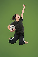 Image showing Forward to the victory.The young woman as soccer football player jumping and kicking the ball at studio on green