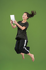 Image showing Image of young woman over green background using laptop computer or tablet gadget while jumping.