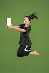 Image showing Image of young woman over green background using laptop computer or tablet gadget while jumping.