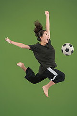 Image showing Forward to the victory.The young woman as soccer football player jumping and kicking the ball at studio on green