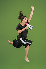 Image showing Beautiful young woman jumping with megaphone isolated over green background