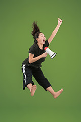 Image showing Beautiful young woman jumping with megaphone isolated over green background