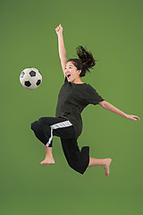 Image showing Forward to the victory.The young woman as soccer football player jumping and kicking the ball at studio on green