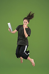 Image showing Image of young woman over green background using laptop computer or tablet gadget while jumping.