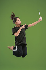 Image showing Image of young woman over green background using laptop computer or tablet gadget while jumping.