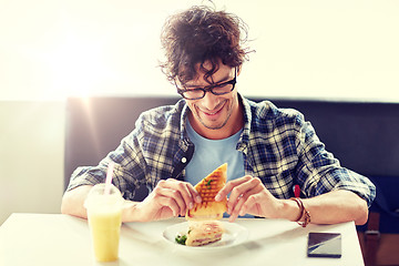 Image showing happy man eating sandwich at cafe for lunch