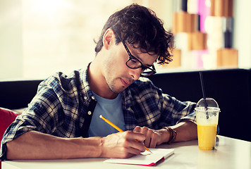 Image showing man with notebook and juice writing at cafe