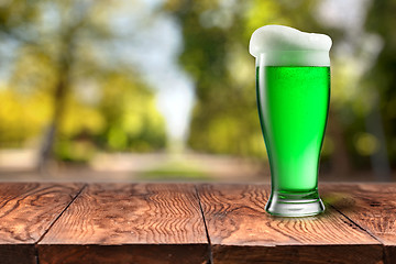 Image showing Green beer in glass on wooden table against blurred park.