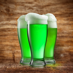 Image showing Alcoholic green beer in the glasses on a blurred wooden.